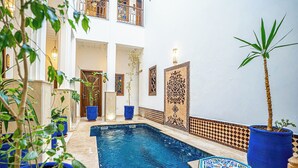 Zona de piscina con suelo de baldosas, plantas en macetas y una pared decorativa.