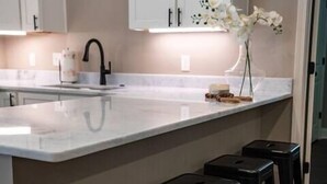 Una cucina moderna con mobili bianchi, una grande isola con sgabelli e un vaso con fiori.