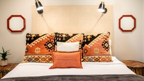 Un letto rifatto con cuscini decorati, due lampade a parete e specchi decorativi su entrambi i lati.