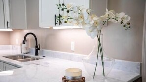 Cucina con mobili bianchi, lavello in acciaio inossidabile e un vaso con fiori bianchi sul bancone.