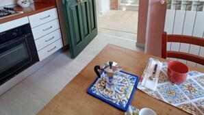 A kitchen with a stove, oven, and cabinets, a table with a coffee pot and cups, and a door leading to a balcony with plants. - A cozy refuge in the sky (tramonti)