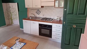 A compact kitchen with white cabinets, a stove, and a sink. A green door is visible on the right. - A cozy refuge in the sky (tramonti)