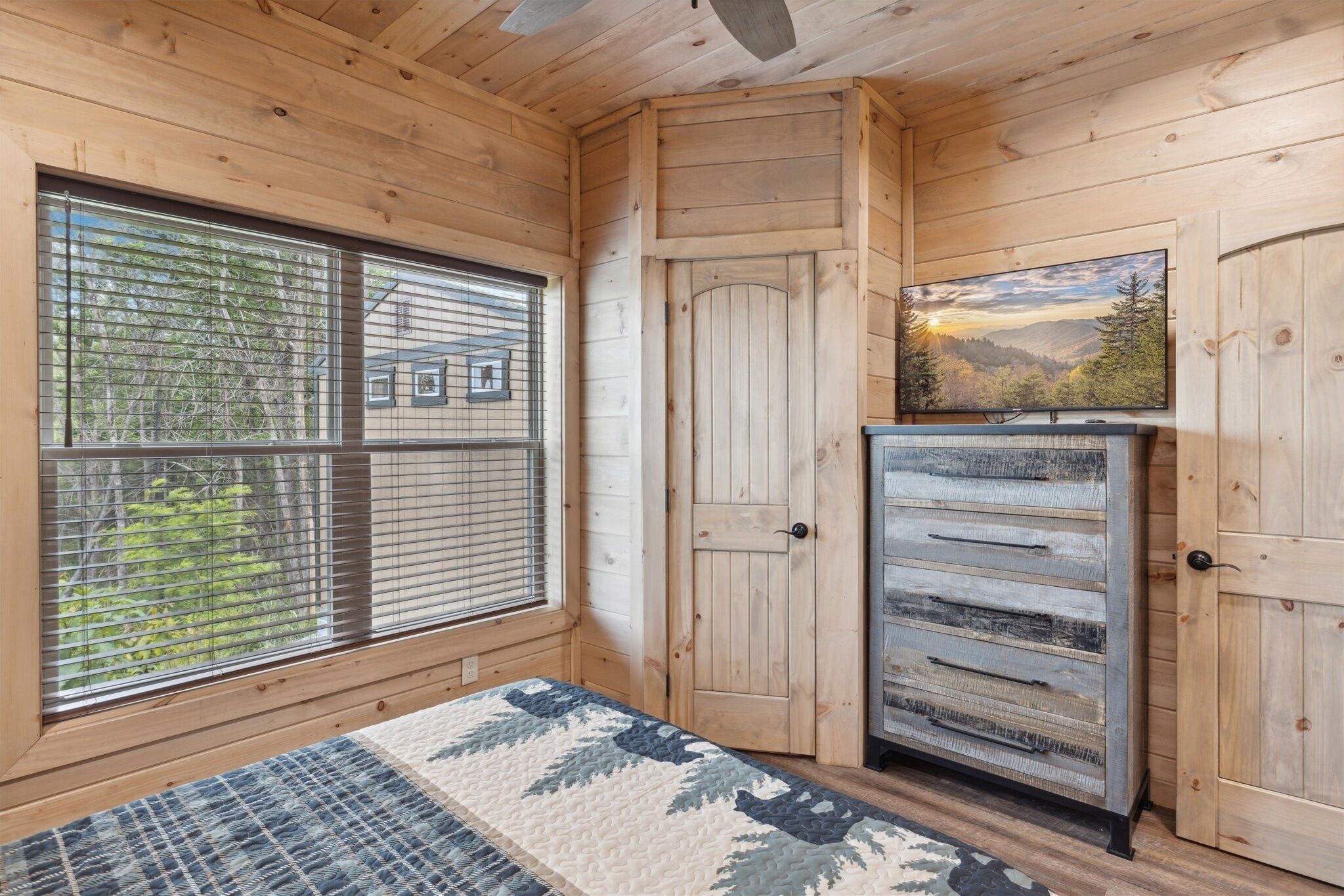Ein Zimmer in einer Holzhütte mit einem Bett, einem Fernseher und einer Tür.