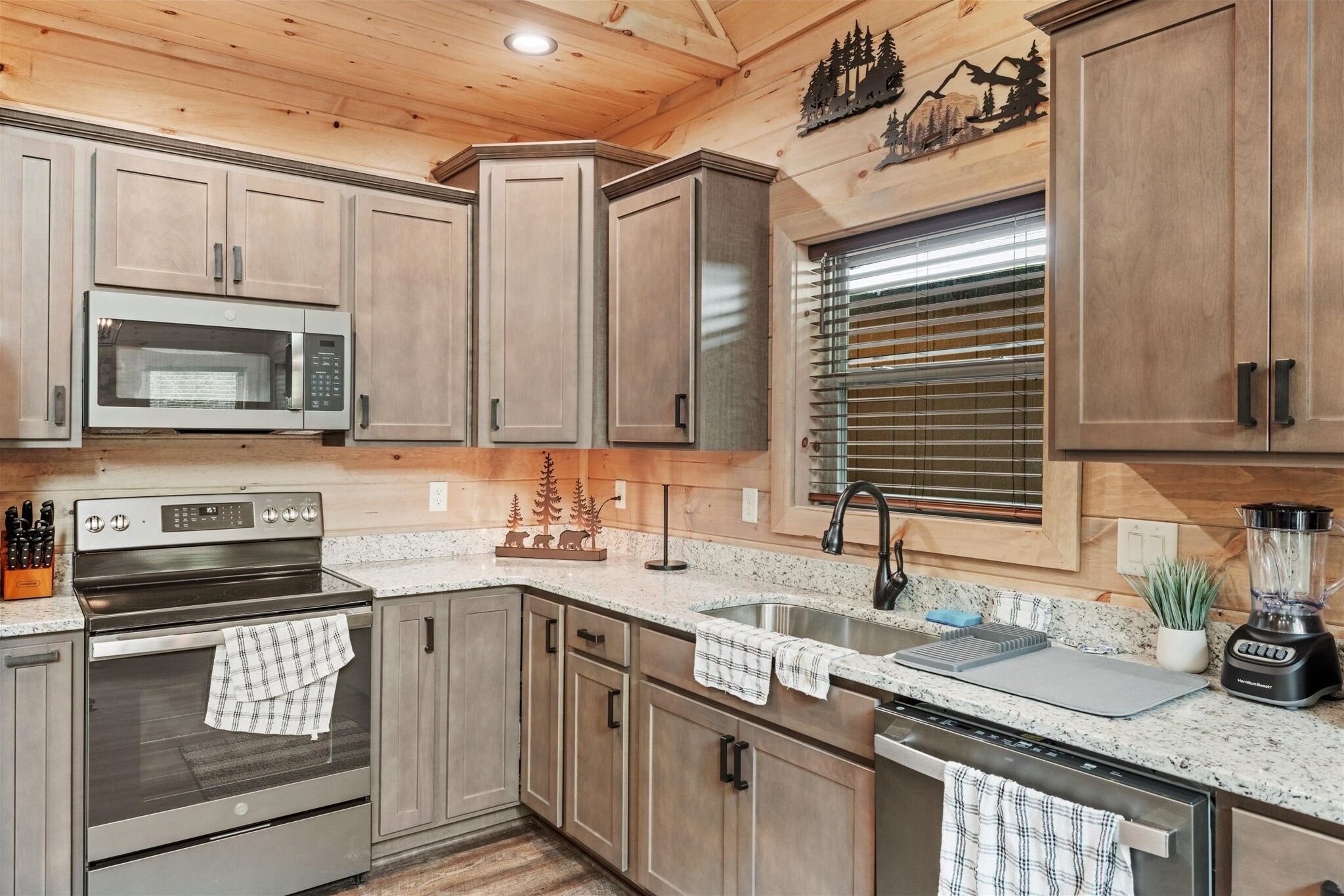 A modern kitchen with wooden cabinets, stainless steel appliances, a granite countertop, and a window with blinds.