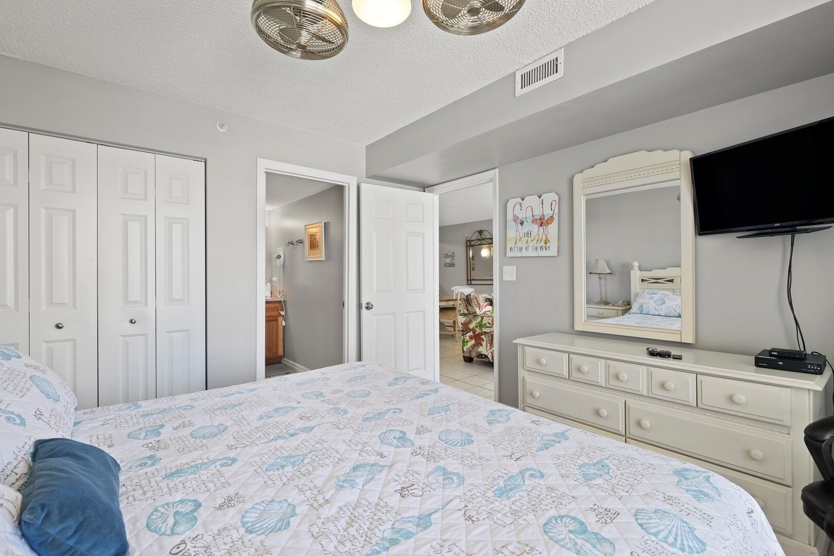 A bedroom with a bed, dresser, TV, and a door leading to another room.