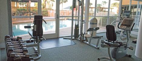 A gym with exercise equipment, a pool, and a view of palm trees.