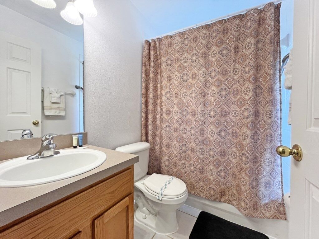 A bathroom with a white sink, wooden vanity, and a patterned shower curtain.