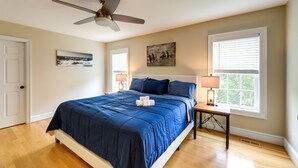 A bedroom with a bed, a ceiling fan, two windows with blinds, a nightstand with a lamp, and artwork on the walls. - Harkers Island Vacation Rental with Pool Table! (Harkers Island)