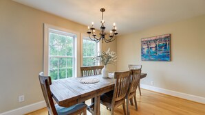 A dining room with a wooden table and chairs, a chandelier, a vase with plants, and a painting on the wall. - Harkers Island Vacation Rental with Pool Table! (Harkers Island)
