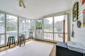 A sunroom with large windows, a white rug, two bar stools, and a metal table.