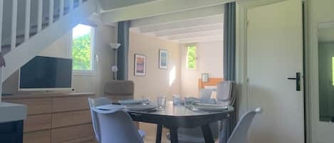 A modern dining area with a round table, four chairs, and a television on a stand.