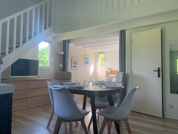 A modern dining area with a round table, four chairs, and a television on a stand.