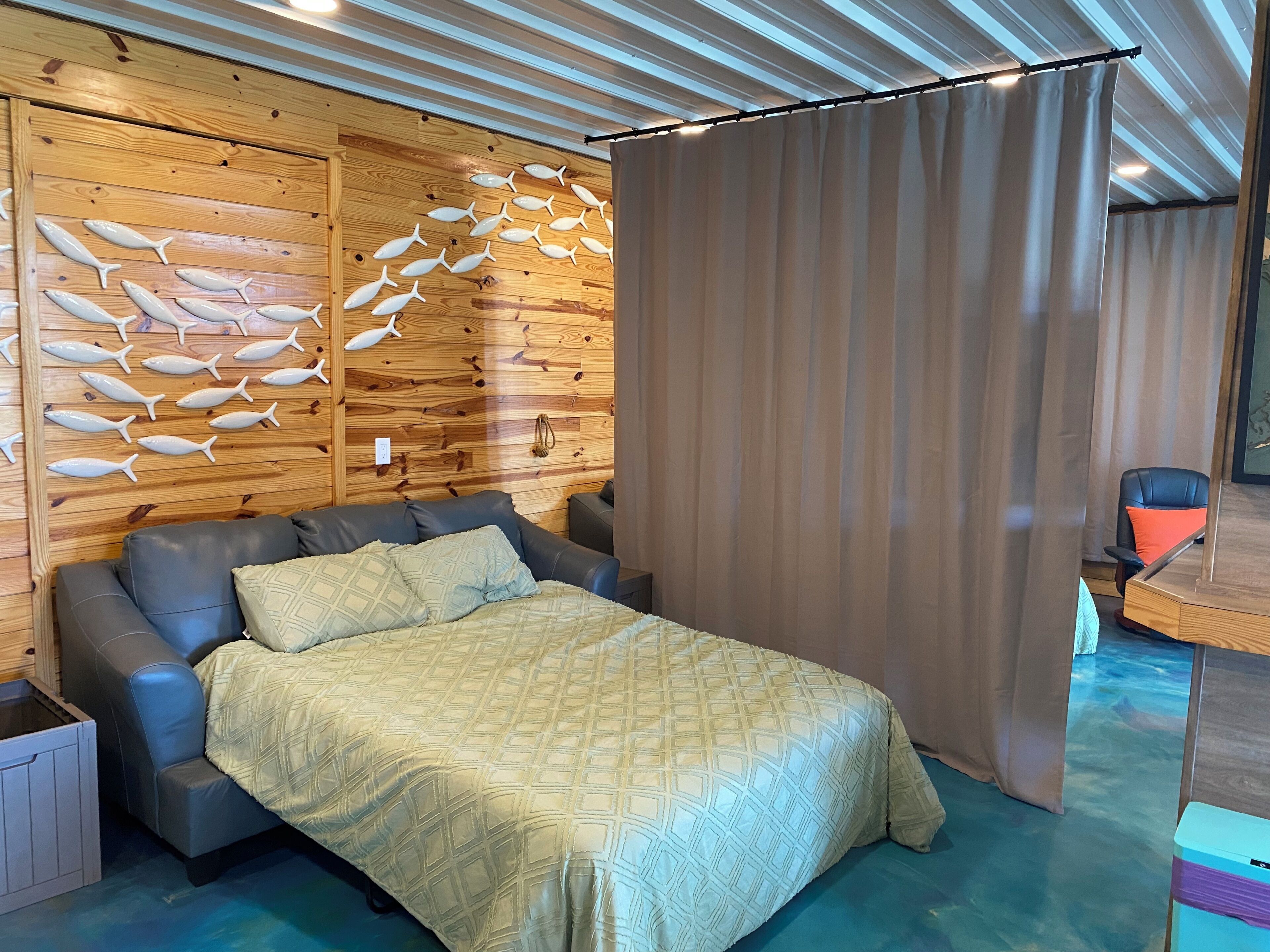 Une pièce avec un lit, un mur en bois décoré de motifs de poissons, un rideau et une chaise.