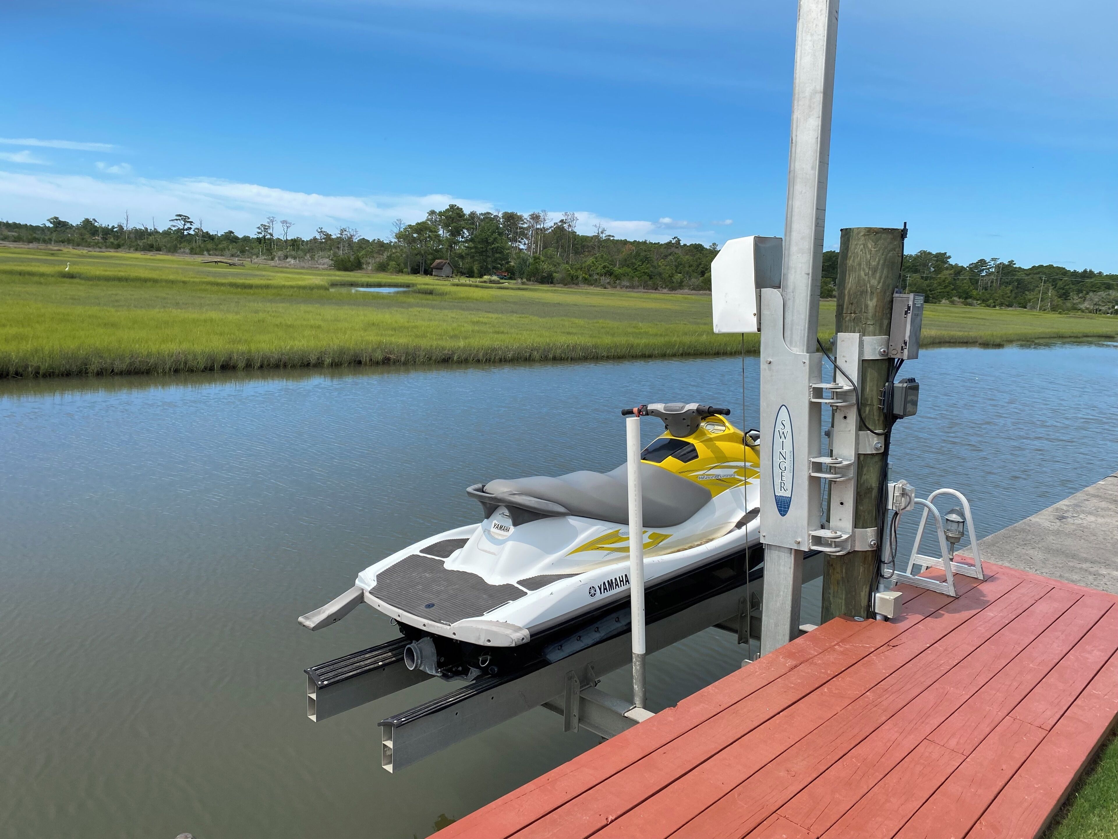 A jet ski docked at a wooden pier with a clear view of a calm water body and a grassy landscape in the background.