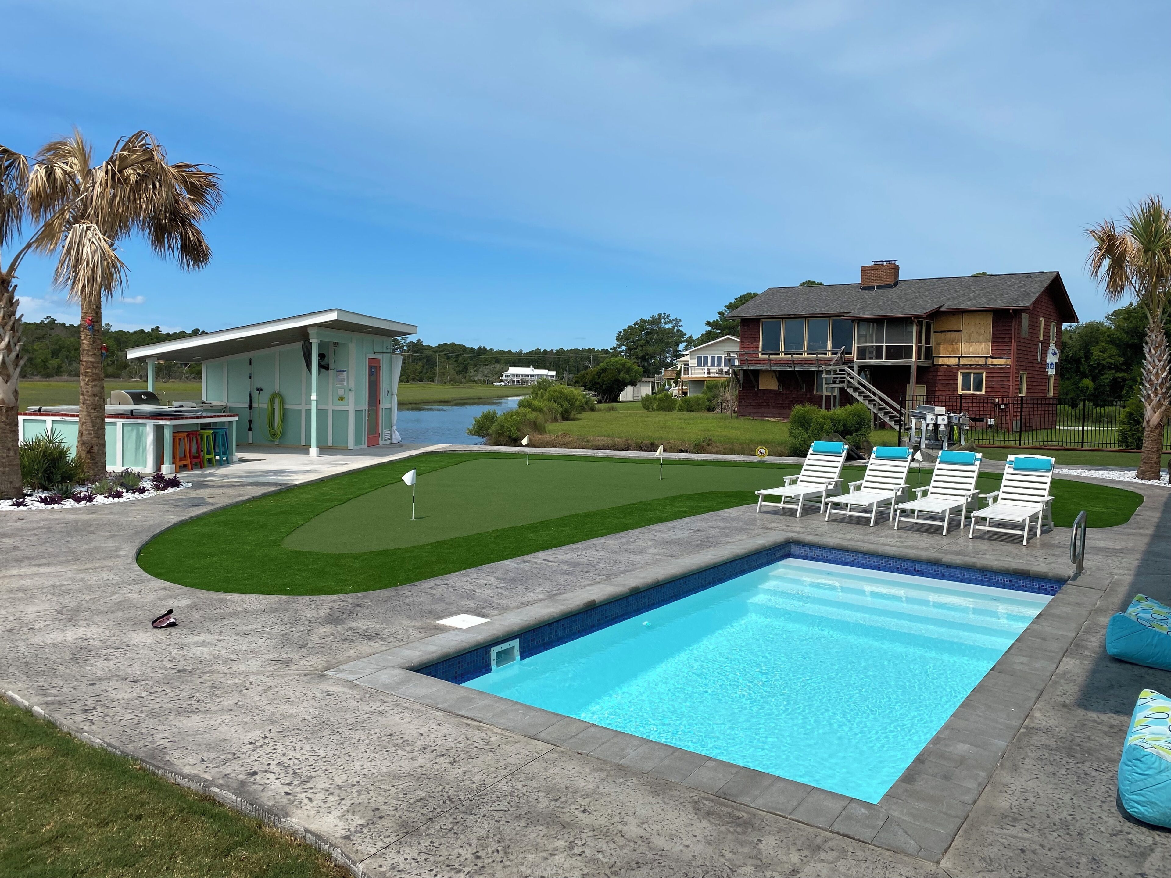 A swimming pool with lounge chairs, a barbecue area, and a view of a lake and houses.