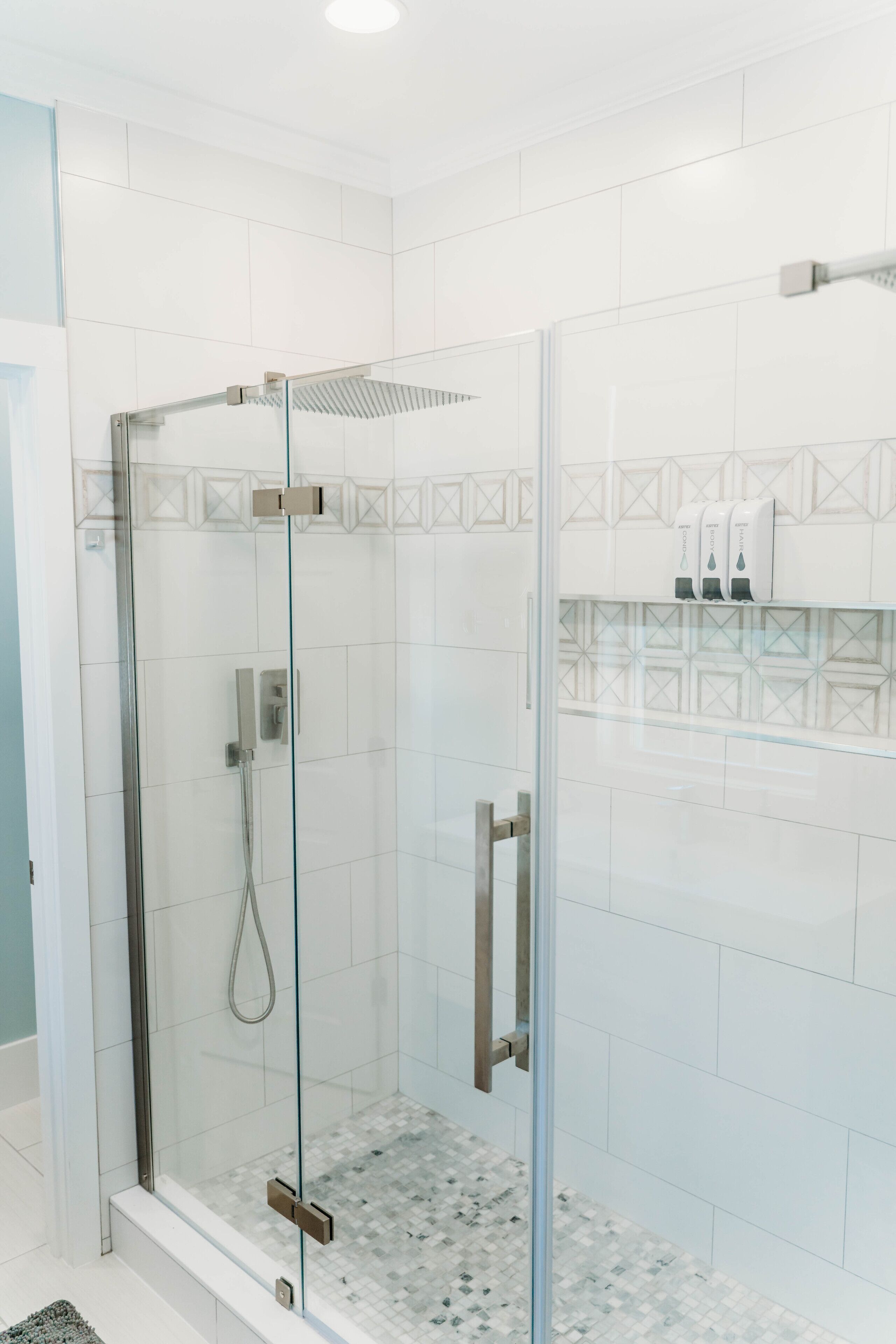 A modern shower with a glass enclosure, a handheld showerhead, and a handheld shower control.