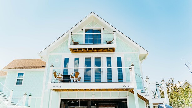 A two-story building with a balcony on the upper floor, a garage at the ground level, and a clear blue sky in the background. - Waterfront with spectacular views, peaceful and private duplex, fishermens dream (Beaufort NC)