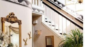 Una escalera con barandilla blanca, un espejo con marco dorado y un candelabro.