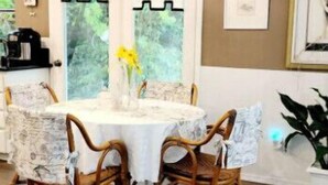 Un comedor con una mesa redonda, cuatro sillas de mimbre, un mantel blanco y una lámpara de araña grande.