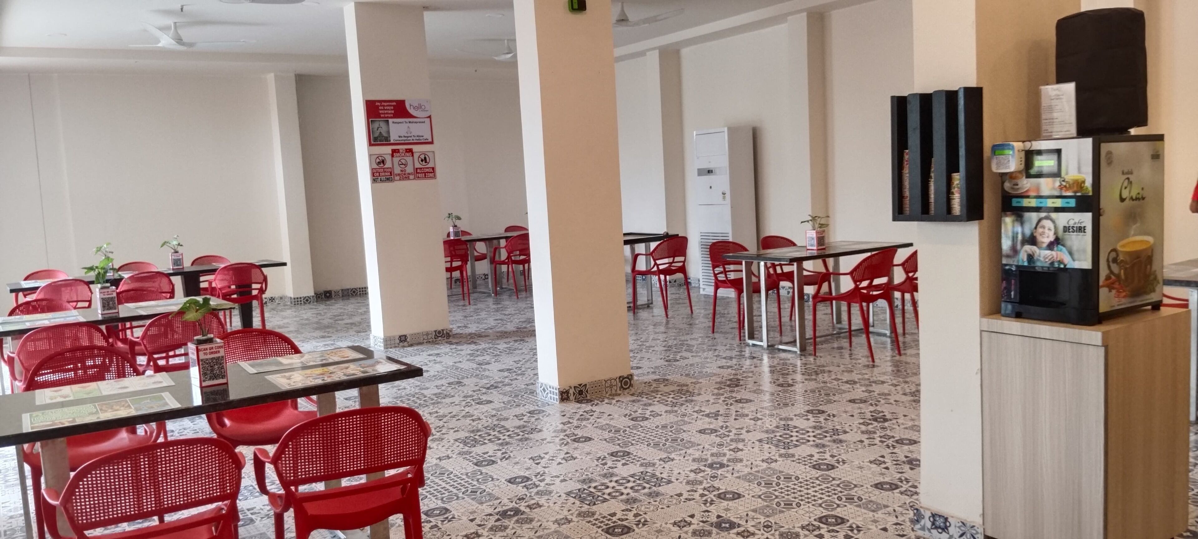 Egy tágas étkező, piros székekkel és asztalokkal, egy vizes adagolóval és egy hűtőszekrénnyel.