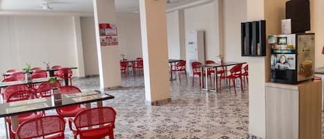 A spacious dining area with red chairs and tables, a water dispenser, and a refrigerator.