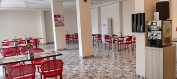 Egy tágas étkező, piros székekkel és asztalokkal, egy vizes adagolóval és egy hűtőszekrénnyel.