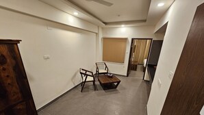 Ein Flur mit einem Holzkasten, einem Stuhl, einem kleinen Tisch und einem Fenster mit Jalousie.