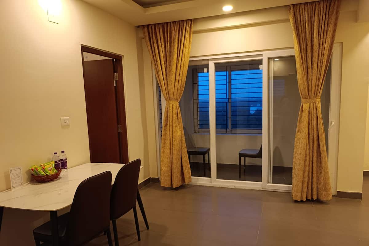 Un área de comedor con una mesa, sillas, una cesta de bocadillos y una ventana con cortinas.
