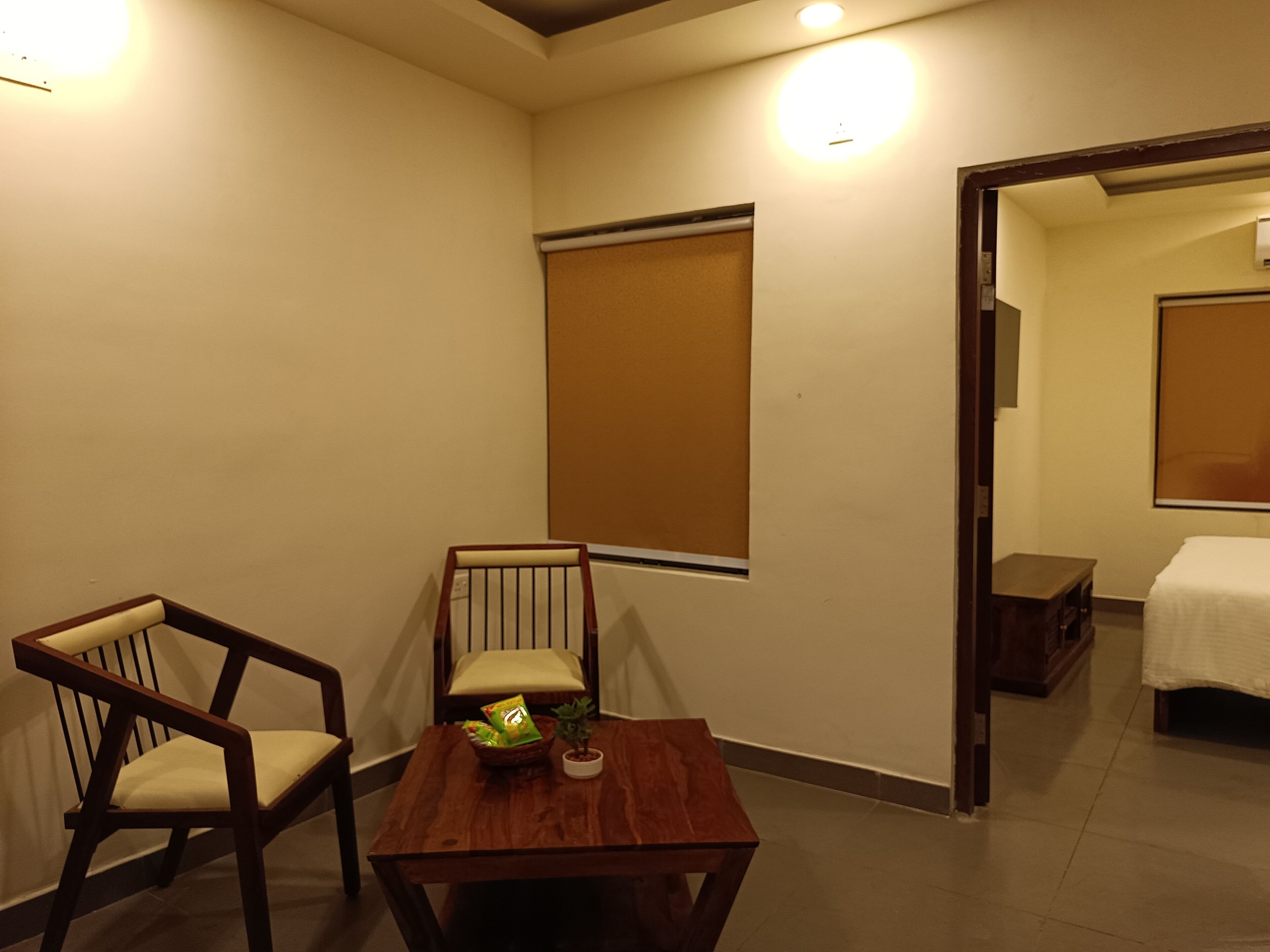 Una habitación con una mesa de madera, dos sillas, una pequeña planta en maceta y una ventana con persiana.