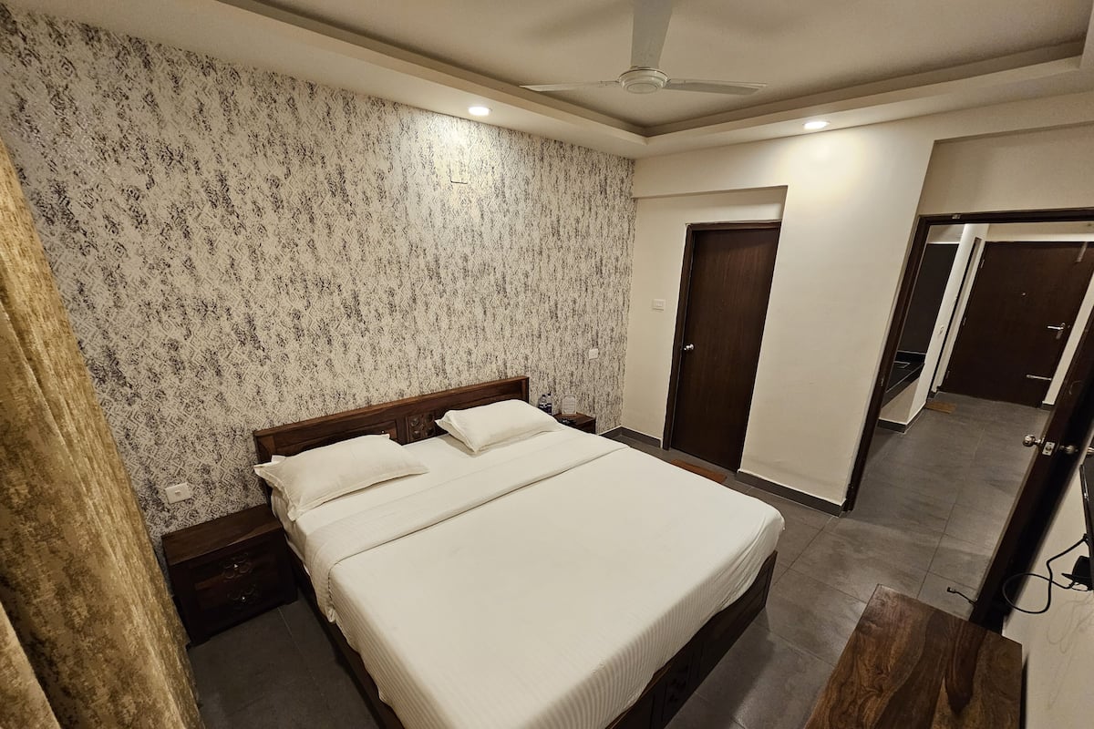 Una cama bien hecha en una habitación de hotel con papel tapiz estampado, cabecero de madera y ventilador de techo.