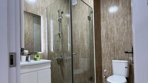 Un baño moderno con cabina de ducha de vidrio, inodoro y tocador con espejo.