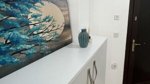Un pasillo con un mostrador de recepción blanco, un cuadro de un árbol, un jarrón y una puerta oscura.