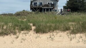 Una casa sulla spiaggia a due piani con un terrazza in legno e una scala che conduce al piano superiore.