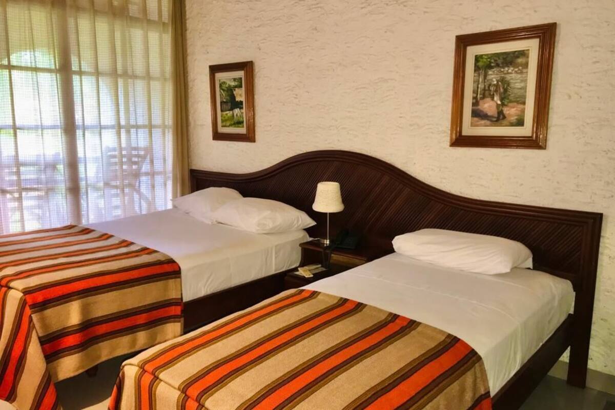 Une chambre d’hôtel avec deux lits, chacun doté d’une literie à rayures, d’une tête de lit en bois et d’une table de chevet avec une lampe.