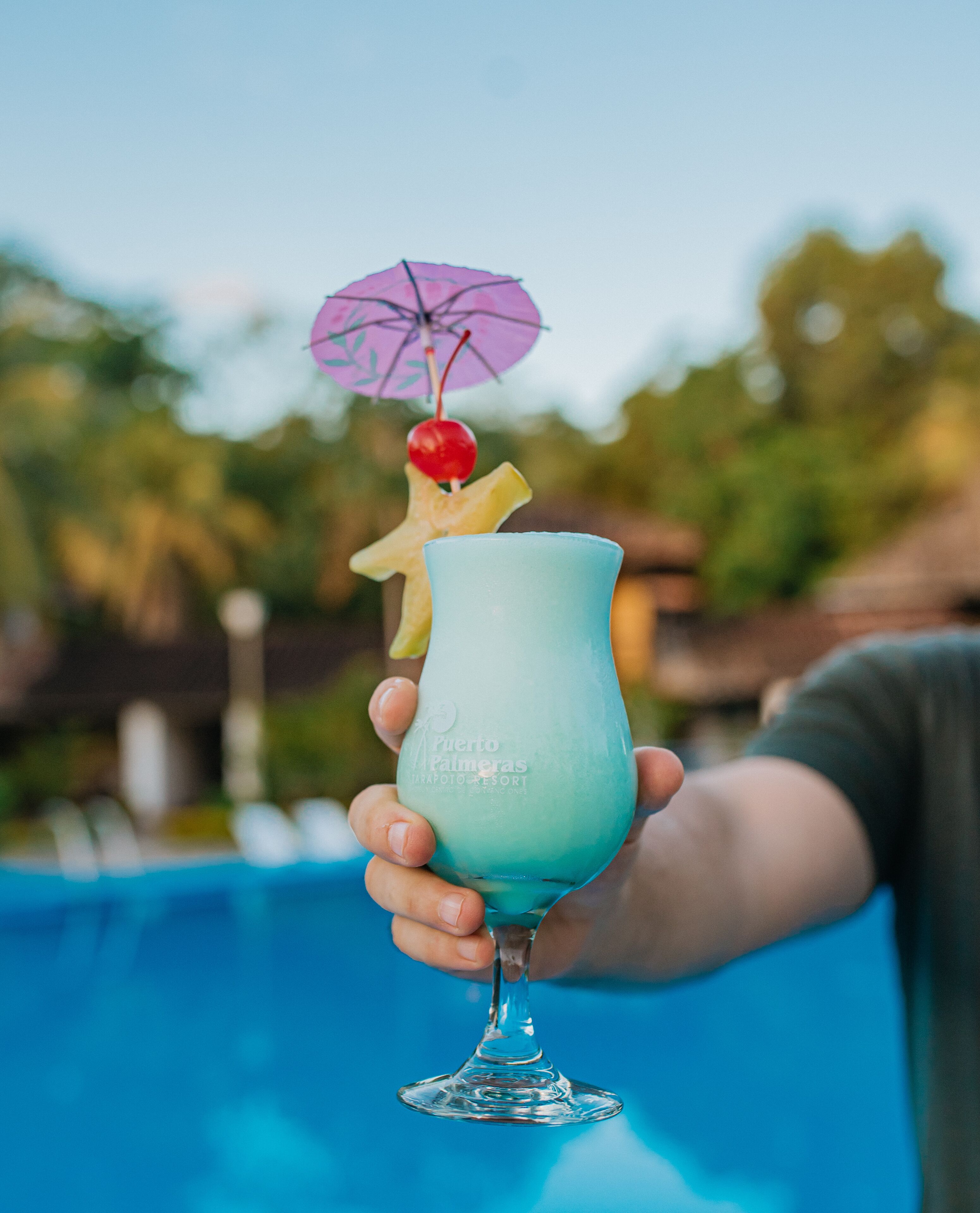 A hand holding a cocktail glass with a tropical design, a cherry, and a small umbrella.