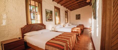 A room with four beds aligned in a row, wooden beams on the ceiling, and a rustic stone wall.