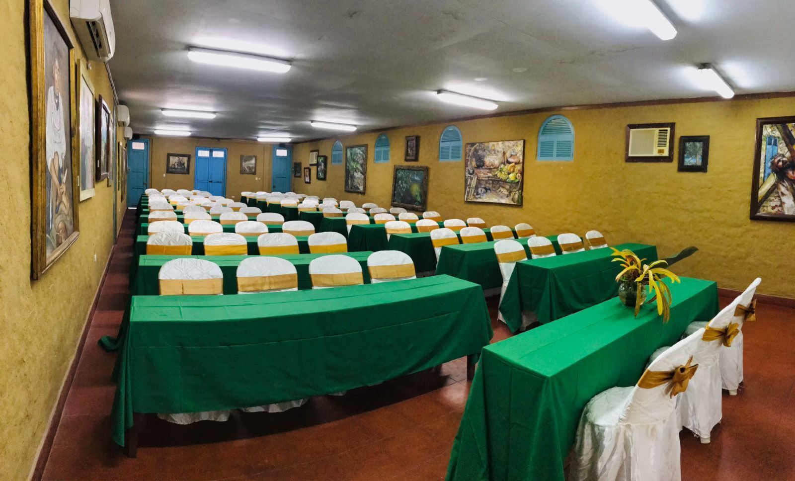 Une salle de conférence avec des rangées de tables recouvertes de nappes vertes et des chaises blanches ornées de rubans jaunes.