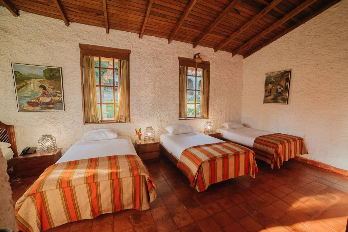 Une chambre avec trois lits, des poutres en bois au plafond et deux tableaux accrochés aux murs.