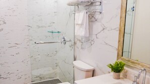 Een moderne badkamer met een douchecabine van glas, een toilet, een wastafel met spiegel, en een klein plantje op de wastafelmeubel.