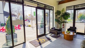 Een hotellobby met grote glazen deuren, zithoekjes binnen en een potplant.
