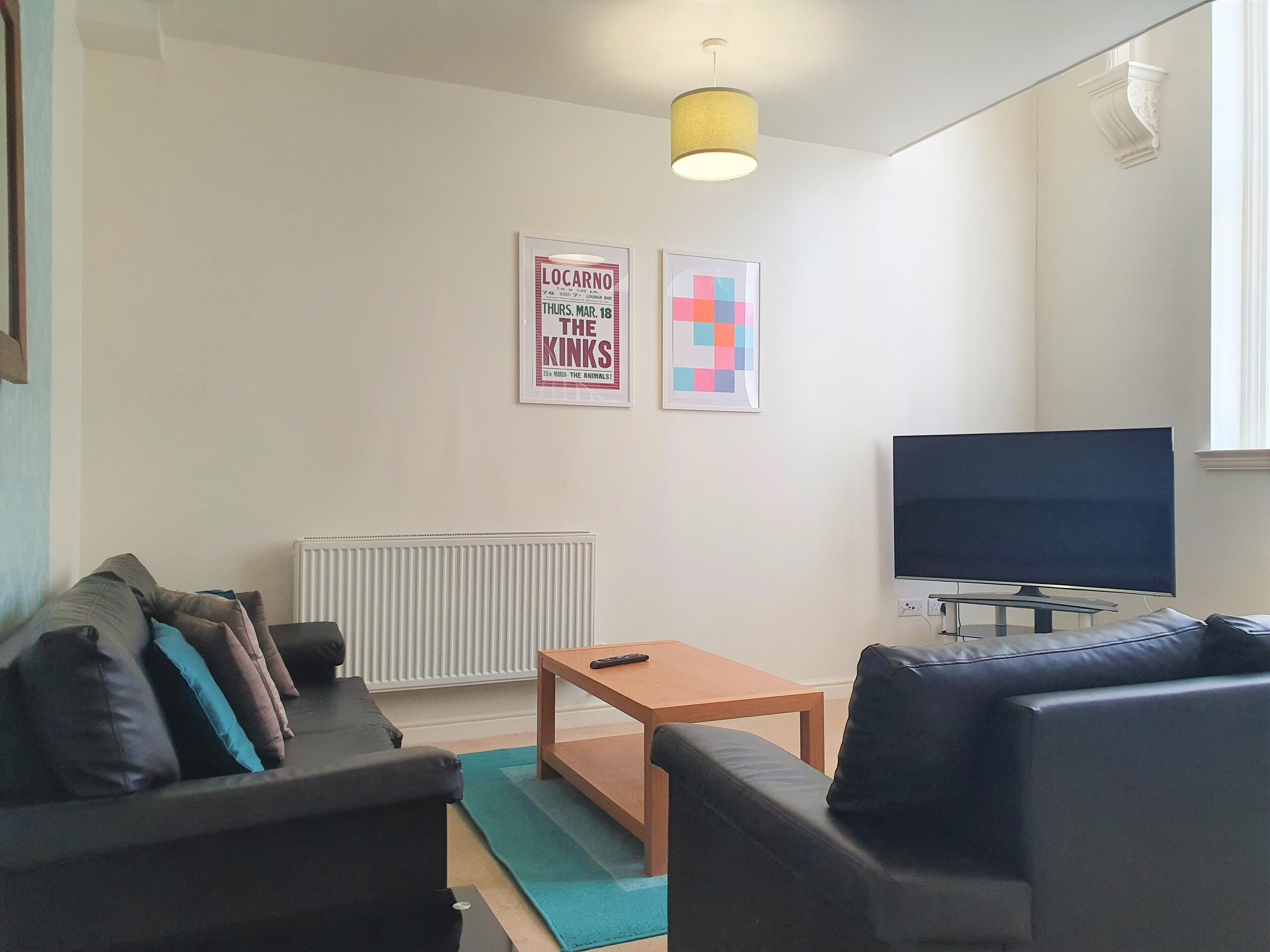Una sala de estar moderna con un sofá, una mesa de centro, un televisor y dos carteles enmarcados en la pared.