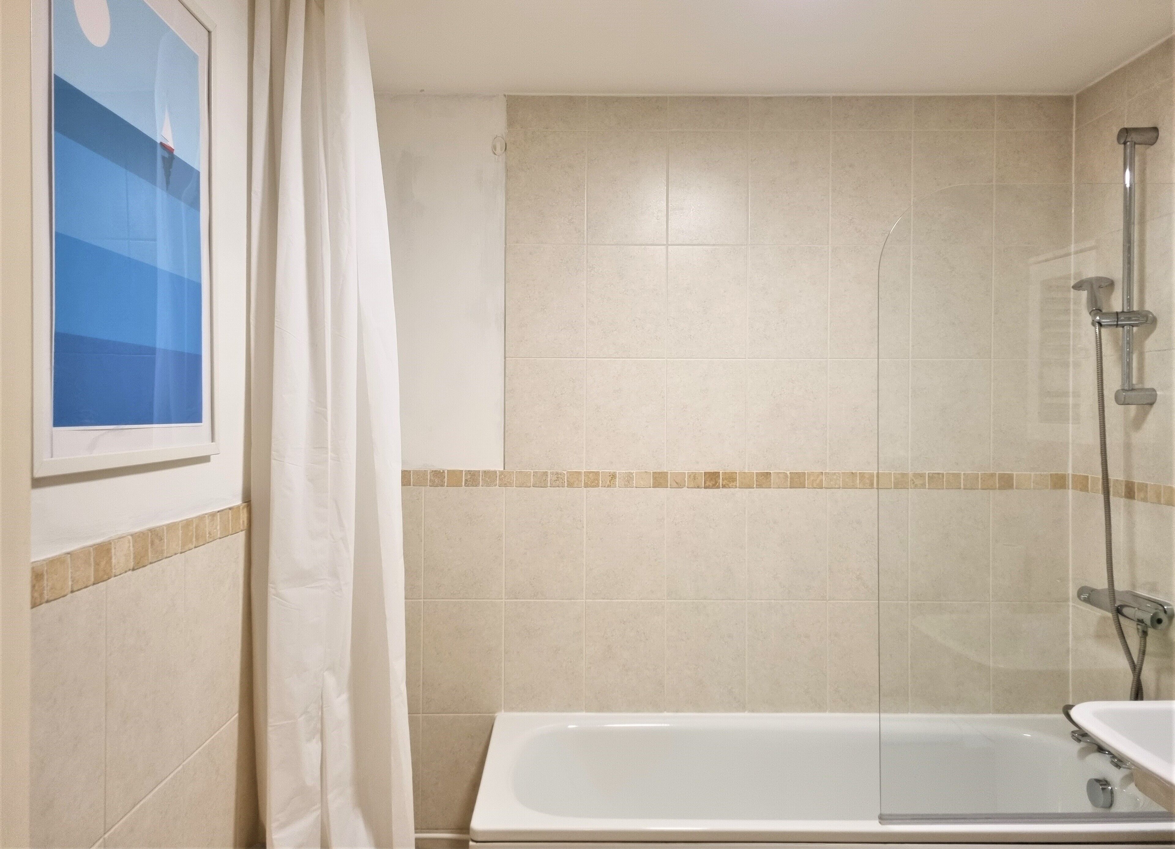 A bathroom with a bathtub, shower, and a framed picture on the wall.