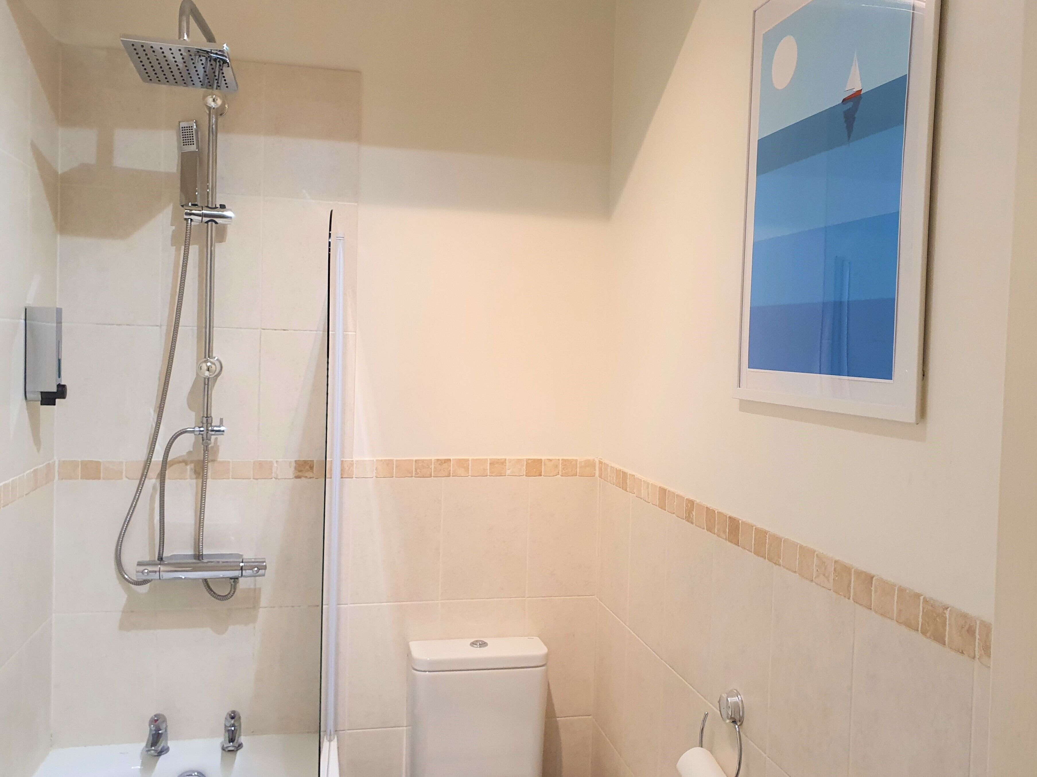 A bathroom with a shower, toilet, sink, and a framed picture on the wall.