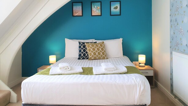 Un lit bien fait, avec du linge de lit blanc, deux lampes de chevet et un mur d’accent bleu orné de trois tableaux encadrés.