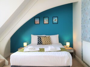Ein ordentlich gemachtes Bett mit weißen Bettwäsche, zwei Nachttischlampen und einer blauen Wand mit drei gerahmten Bildern.