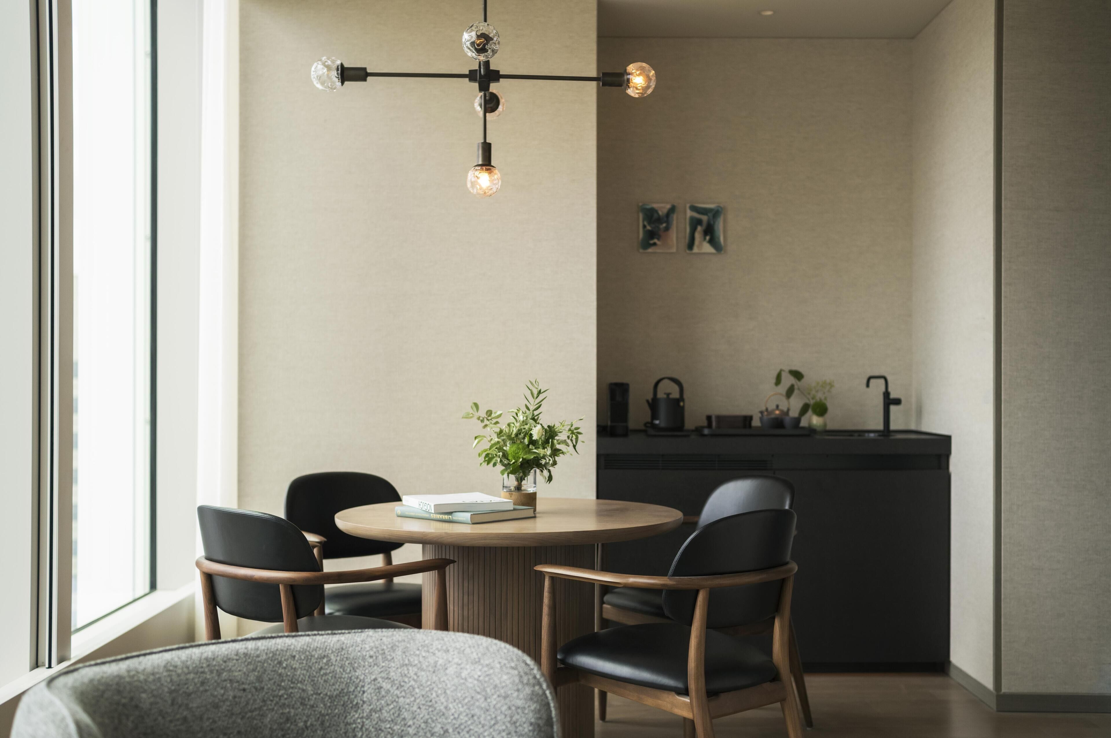 Un comedor moderno con una mesa redonda, dos sillas, una lámpara colgante y una cocina al fondo.