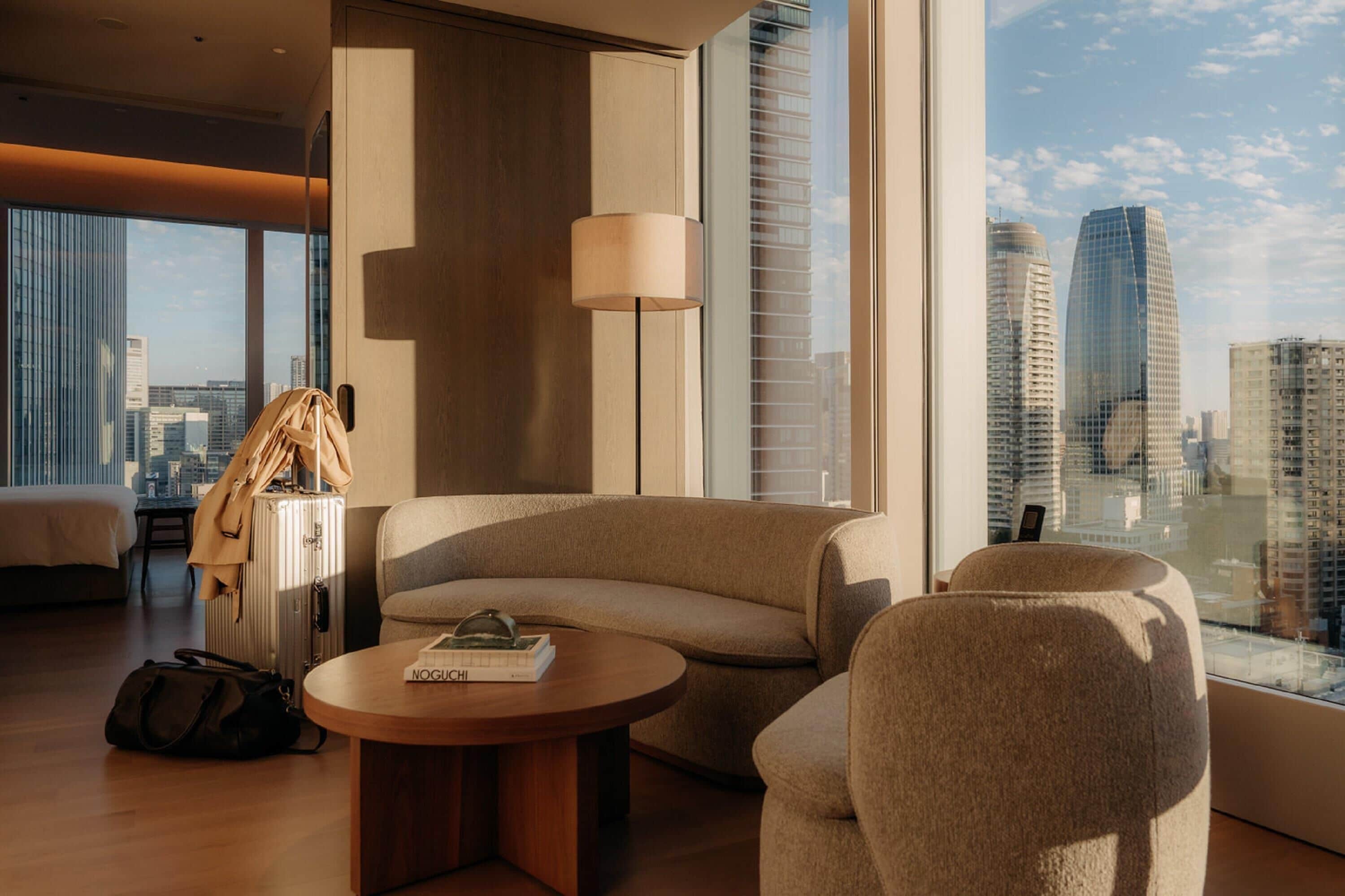 Una habitación de hotel moderna con un ventanal grande, un sofá, una mesita y una lámpara.