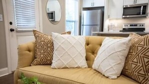 A beige sofa with patterned cushions in a modern living room with a kitchen in the background. - The Paige, Cozy 1BR Studio by Velvet Ditch Villas (Oxford)