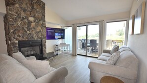 Una sala de estar con chimenea de piedra, televisor de pantalla plana, sofá blanco y cesta de mimbre.