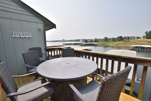 Una terrazza con un tavolo rotondo e sedie, affacciata su uno specchio d'acqua con pontili e edifici all'orizzonte.